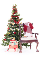 Empty chair with blanket on it near Christmas tree and stack of gift boxes on white background