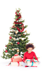 Portrait of cute mixed race little boy sitting on floor near Christmas tree with gift box in his hands