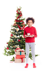 Portrait of cute mixed race little boy standing near Christmas tree with plate of cookies and glass of milk