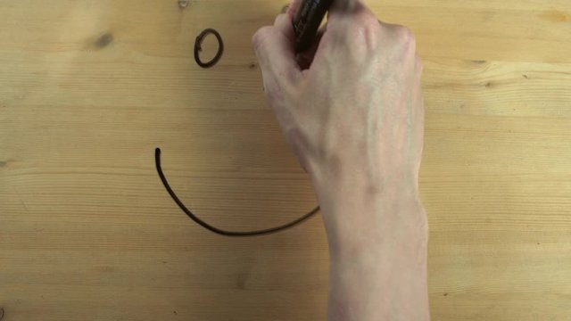 Male hand drawing and wipes out smiley face on wooden surface