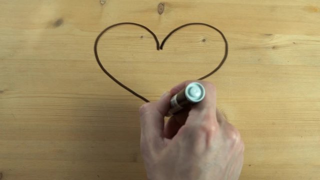 Male hand drawing heart shape and turn it into kissing couple on wooden surface
