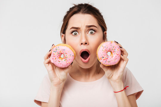 Close up portrait of a shocked pretty girl holding donuts