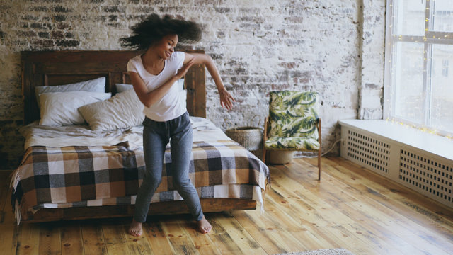 Attractive mixed race young joyful woman have fun dancing near bed at home
