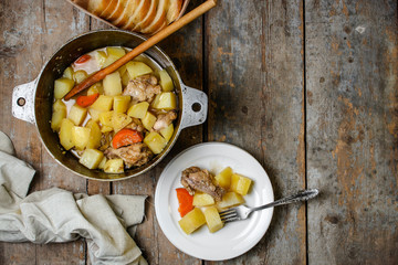 chicken meat stewed with potatoes, carrots and spices in a cast-iron pot on a wooden background