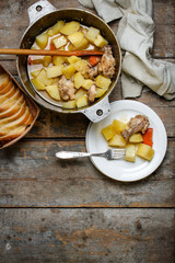 chicken meat stewed with potatoes, carrots and spices in a cast-iron pot on a wooden background
