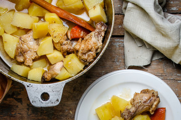chicken meat stewed with potatoes, carrots and spices in a cast-iron pot on a wooden background