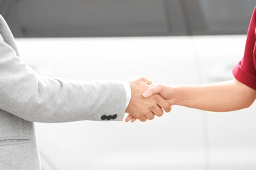 Customer and salesman shaking hands near new car outdoors