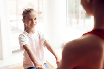 Mother and daughter are engaged in yoga in sportswear. They are in a bright room with panoramic windows.