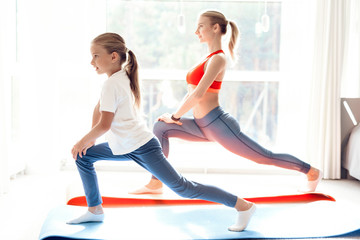 Fototapeta na wymiar Mother and daughter are engaged in yoga in sportswear. They are in a bright room with panoramic windows.