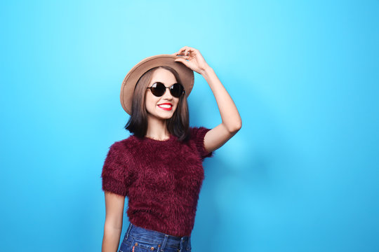 Attractive hipster girl with hat and sunglasses on color background