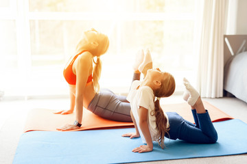 Mother and daughter are engaged in yoga in sportswear. They are in a bright room with panoramic windows