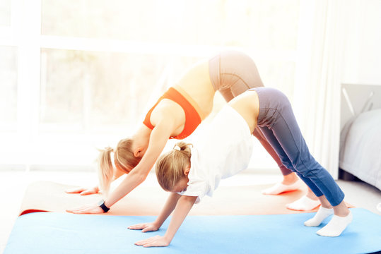 Mother and daughter are engaged in yoga in sportswear. They are in a bright room with panoramic windows.