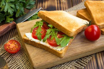 Vegetarian sandwich with tomato and arugula on the wooden cutting board