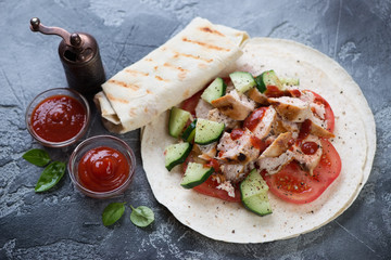 Shaurma or roasted chicken meat with fresh vegetables served on tortilla bread. Dark grey stone surface, studio shot