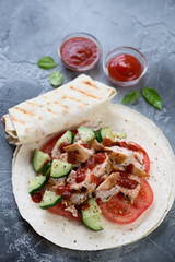 Shawarma or shaurma with roasted chicken and fresh vegetables wrapped in tortilla, selective focus, studio shot