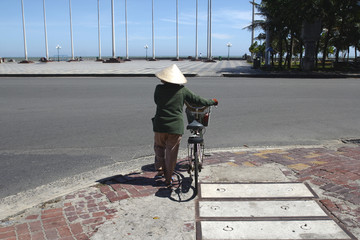 Fototapeta na wymiar Vietnamese woman in a national hat with a bicycle crosses the road