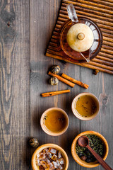 Tea ceremony concept. Tea pot on bamboo mat, cups, dry tea leaves, sugar on dark wooden background top view copyspace
