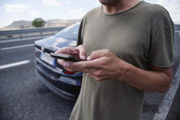 man using a smartphone next to a car on the road