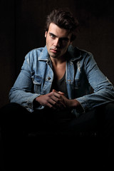 Handsome male model posing in fashion blue jeans jacket looking on dark shadow background. Closeup portrait