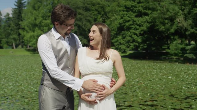SLOW MOTION CLOSE UP: Expecting parents smile as they feel their baby kicking for the first time. Man and woman lovingly gaze at each other. Smiling husband and wife enjoy the wonders of pregnancy.