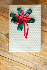 White gift box and red ribbon  on wood background with space..