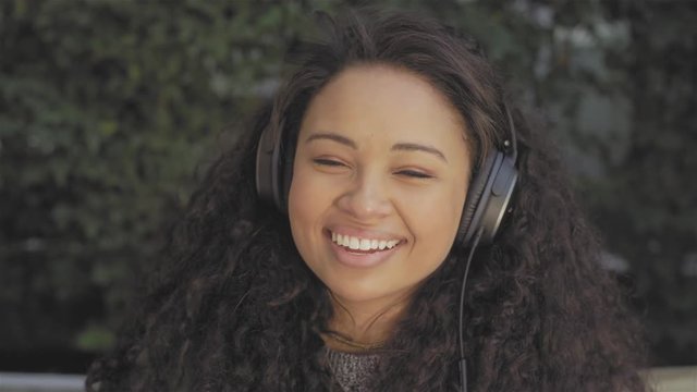 Close up shot of a beautiful young woman listening to music with headphones. She then begins to laugh