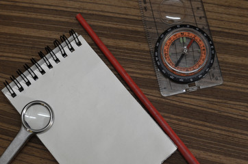 notepad pencil Compass with a transparent ruler and  Magnifying glass on wood sheet close up