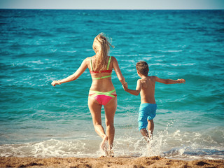 Naklejka premium Caucasian woman and son running into the sea water. Back view.