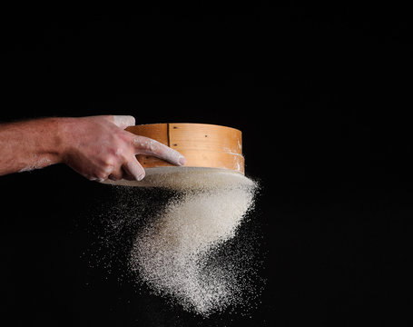men's hands are sifting flour through a sieve on black background