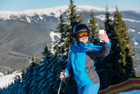 Close up shot of a woman skier smiling taking a selfie with her smart phone while skiing in the mountains at the ski resort on a sunny winter day technology connectivity mobility sport recreation