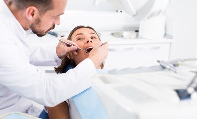 Dentist is treating female patient which is sitting in dental chair