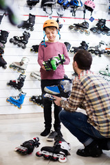 male seller putting roller-skates on boy customer in sports store