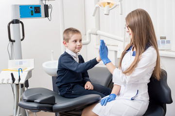 Smiling kid giving five to female dentist in dental clinic. Young boy on dental check up