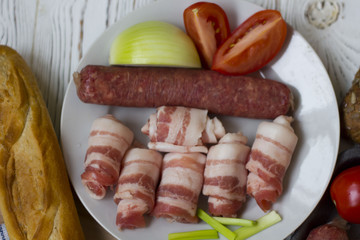sausages, bacon, vegetables and bread on white wooden table
