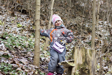 Cute six year old girl dressed in pink hat, boots and overalls and pink bag in the winter forest