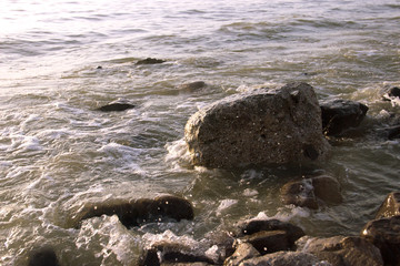 View of dawn at the seaside with the clear sky. surf waves and large boulder stones. Blue background with copy space