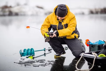 Selbstklebende Fototapeten Man ice fishing on a frozen lake. © kaninstudio