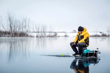 Zelfklevend Fotobehang Man ice fishing on a frozen lake. © kaninstudio