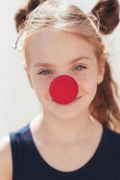 portrait of a little girl with a clown nose on the street