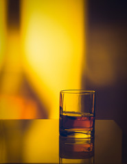 Single glass of whisky whiskey bourbon on ice on top of a wood bar table and wooden background