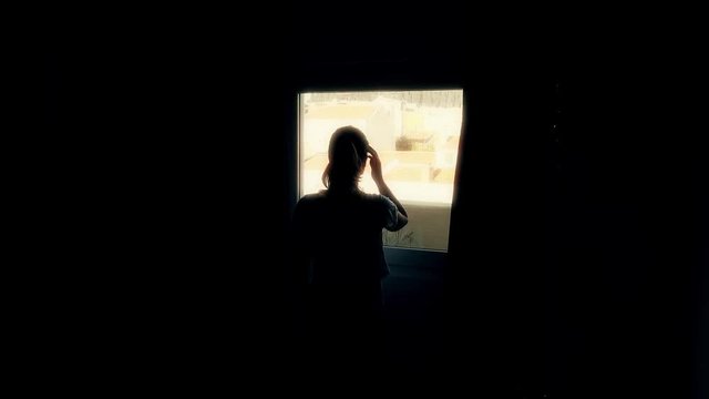 Backlit Woman Opens Curtains In Bedroom. Silhouette of woman opening the curtains of bedroom on a sunny morning