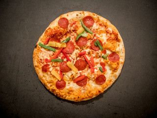 Top view of salami pizza on dark background.
