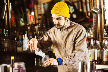Portrait of hipster barman adding ice cubes to a cocktail at bar background.