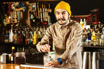 Portrait of hipster barman mixing a cocktail with a spoon at bar background.