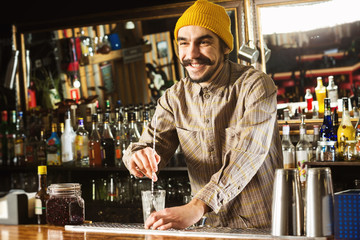 Portrait of hipster barman mixing a cocktail with a spoon at bar background.