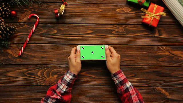 Top view on woman hands holding the white smart phone horizontally, Christmas decoration, green screen, chroma key, tracking motion