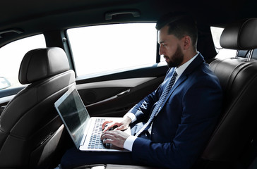 businessman using a laptop in the backseat of a car