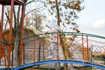 Little girl is playing on the playground in the park. The child goes on the steps of the playground.