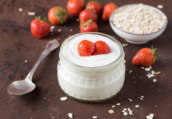 White yogurt in glass bowl with spoon and starwberries on rustic background.