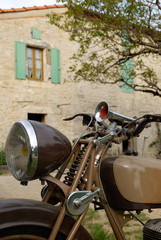 Old brown motorcycle in front of old stoned house